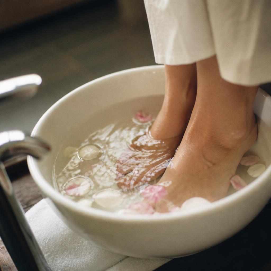 Feet soaking in a pedicure bowl with floating flower petals